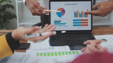 İş adamları masadaki bir grafiği analiz etmek için ekrandaki verileri tartışıyor ve analiz ediyorlar..