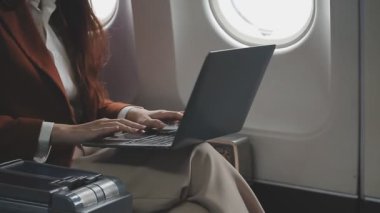 Genç iş kadını dizüstü bilgisayar kullanıyor ve uçakta daktilo yazıyor..