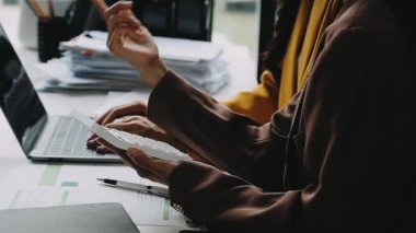 Genç Asyalı iş kadını, modern bilgisayarla ofis masasında otururken dizüstü bilgisayar ve akıllı telefon kullanıyor.