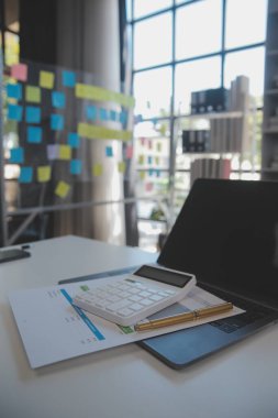 Close up view of simple workspace with laptop, notebooks, coffee cup and tree pot on white table with blurred office room background