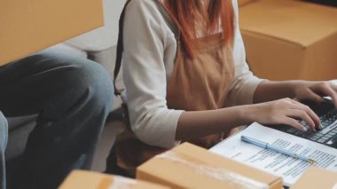 Asyalı genç bayan dizüstü bilgisayarla çalışıyor ve ofiste karton paketliyor. Online nakliye işi konsepti. dağıtım servisi.