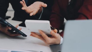 Genç adam ofiste dizüstü bilgisayar ve akıllı telefonla çalışıyor.