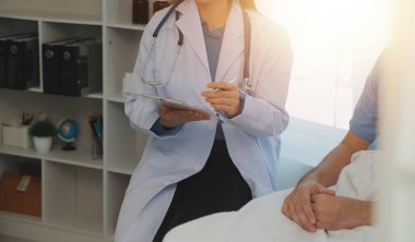 Genç doktor steteskop kullanıyor. Hastanın kalp atışlarını dinle. Kadın bir doktorun erkek bir hastaya muayene yaparken görüntüsü.