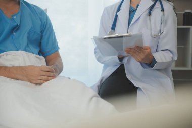 Genç doktor steteskop kullanıyor. Hastanın kalp atışlarını dinle. Kadın bir doktorun erkek bir hastaya muayene yaparken görüntüsü.