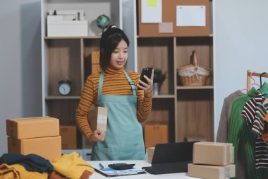 Vlogger, blog yazarı, küçük KOBİ iş kadını güzel bir kadın cep telefonuyla kıyafetleri satıyor canlı yayın satışı yapıyor, ana ofiste ürün sunumu detaylarını gösteriyor, girişimci ekommerce