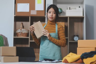 Vlogger, blog yazarı, küçük KOBİ iş kadını güzel bir kadın cep telefonuyla kıyafetleri satıyor canlı yayın satışı yapıyor, ana ofiste ürün sunumu detaylarını gösteriyor, girişimci ekommerce