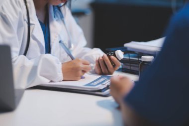 Ofiste çalışan ve hastayı dinleyen doktor semptomlarını, sağlık hizmetlerini ve yardım kavramlarını açıklıyor.