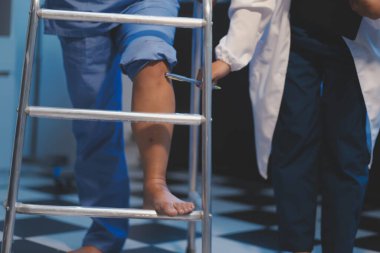 Asyalı, genç, profesyonel, dost canlısı mavi hastane üniformalı kadın hemşire yaşlı, yaşlı, sağlıksız, dört bacaklı, yürüyen bir hastanın fiziksel terapisine yardım ediyor..