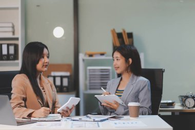 Two young Asian business woman talk, consult, discuss working with new startup project idea presentation analyze plan marketing and investment in the office.