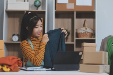 Vlogger, blog yazarı, küçük KOBİ iş kadını güzel bir kadın cep telefonuyla kıyafetleri satıyor canlı yayın satışı yapıyor, ana ofiste ürün sunumu detaylarını gösteriyor, girişimci ekommerce