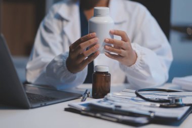 Doktor ilaç şişesini tutuyor ve ofiste notlar alıyor..