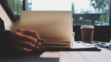 İş adamı iş yerindeki masada otururken deftere yazı yazıyor.