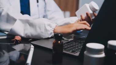 Ofisteki doktor. Doktor masada oturuyor ve elinde bir dizüstü bilgisayar ve stetoskop tutuyor..