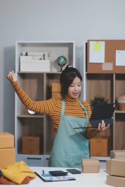 Vlogger, blog yazarı, küçük KOBİ iş kadını güzel bir kadın cep telefonuyla kıyafetleri satıyor canlı yayın satışı yapıyor, ana ofiste ürün sunumu detaylarını gösteriyor, girişimci ekommerce