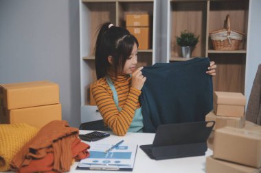 Vlogger, blog yazarı, küçük KOBİ iş kadını güzel bir kadın cep telefonuyla kıyafetleri satıyor canlı yayın satışı yapıyor, ana ofiste ürün sunumu detaylarını gösteriyor, girişimci ekommerce