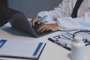 Önlüklü profesyonel ve odaklanmış Asyalı kadın bir doktor hastanede bilgisayarında tıbbi araştırmaları okuyor ve çalışıyor..