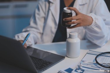 Doktor ilaç şişesini tutuyor ve ofiste notlar alıyor..