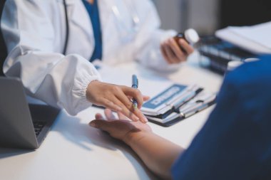 Ofiste çalışan ve hastayı dinleyen doktor semptomlarını, sağlık hizmetlerini ve yardım kavramlarını açıklıyor.