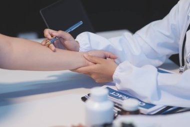 Ofiste çalışan ve hastayı dinleyen doktor semptomlarını, sağlık hizmetlerini ve yardım kavramlarını açıklıyor.