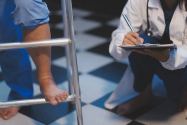 Asyalı, genç, profesyonel, dost canlısı mavi hastane üniformalı kadın hemşire yaşlı, yaşlı, sağlıksız, dört bacaklı, yürüyen bir hastanın fiziksel terapisine yardım ediyor..