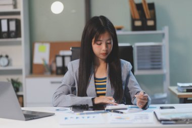 Güzel Asyalı iş kadını, ofise yerleştirilmiş evraklarla birlikte tablet ve dizüstü bilgisayar kullanıyor..