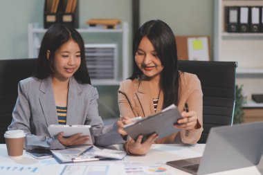 Two young Asian business woman talk, consult, discuss working with new startup project idea presentation analyze plan marketing and investment in the office.