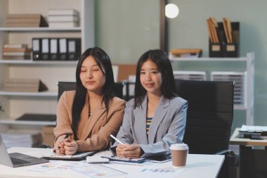 Two young Asian business woman talk, consult, discuss working with new startup project idea presentation analyze plan marketing and investment in the office.