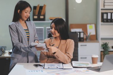 Two young Asian business woman talk, consult, discuss working with new startup project idea presentation analyze plan marketing and investment in the office.