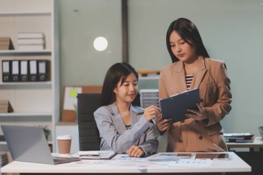 Two young Asian business woman talk, consult, discuss working with new startup project idea presentation analyze plan marketing and investment in the office.