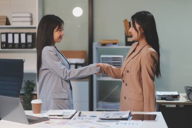 Ofis toplantısı sırasında el ele tutuşan kendine güvenen iki iş kadını. Başarı. Yöneticiler. İş arkadaşları ayakta alkışlıyor. Tebrikler takım çalışması..