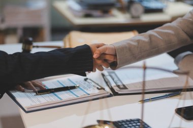 Avukat, müvekkil ile evraklar, sözleşmeler, anlaşmalar, iş birliği anlaşmaları hakkında el sıkışıyor avukatın masasında bir kadın müvekkil ve masada bir çekiç.