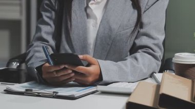 Akıllı telefon tutan ve modern ofisteki masaya notlar yazan bir iş kadını.