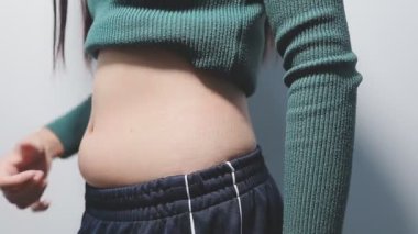 Gri arka planda karnını gösteren genç bir kadın..