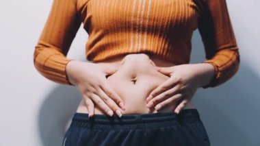 Gri arka planda karnını gösteren genç bir kız.