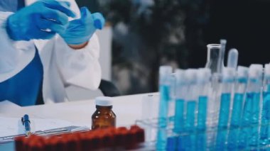 Koruyucu eldivenler giymiş bilim adamı deney tüpleri ve aşıyla matara tutuyor.