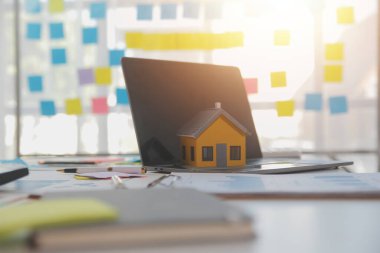 Diz üstü bilgisayarı olan ahşap masa, kalem, ev modeli ve yeşil ağaç hesap makinesi olan ev anahtarları, emlak konsepti. Resimleri kapat