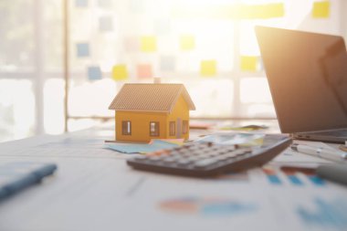 Diz üstü bilgisayarı olan ahşap masa, kalem, ev modeli ve yeşil ağaç hesap makinesi olan ev anahtarları, emlak konsepti. Resimleri kapat