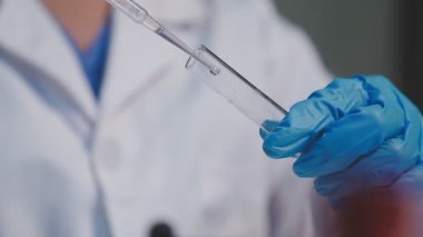 Yakın plan. Laboratuvarda elinde mavi bir tüp tutan doktor eli.