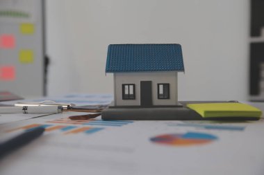 Diz üstü bilgisayarı olan ahşap masa, kalem, ev modeli ve yeşil ağaç hesap makinesi olan ev anahtarları, emlak konsepti. Resimleri kapat