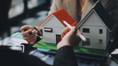 Emlakçı ev modelini tutuyor ve ev modelini gösteriyor.