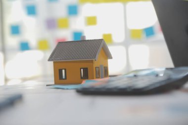 Diz üstü bilgisayarı olan ahşap masa, kalem, ev modeli ve yeşil ağaç hesap makinesi olan ev anahtarları, emlak konsepti. Resimleri kapat