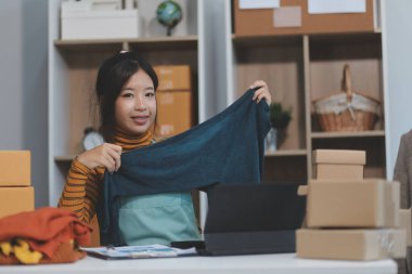 Vlogger, blog yazarı, küçük KOBİ iş kadını güzel bir kadın cep telefonuyla kıyafetleri satıyor canlı yayın satışı yapıyor, ana ofiste ürün sunumu detaylarını gösteriyor, girişimci ekommerce