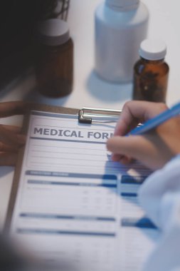 Doktor masasında oturuyor ve hastası için reçete yazıyor.