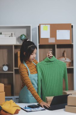 Vlogger, blog yazarı, küçük KOBİ iş kadını güzel bir kadın cep telefonuyla kıyafetleri satıyor canlı yayın satışı yapıyor, ana ofiste ürün sunumu detaylarını gösteriyor, girişimci ekommerce