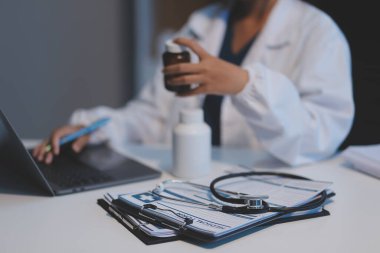 Doktor ilaç şişesini tutuyor ve ofiste notlar alıyor..