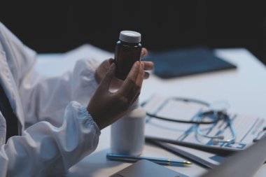Doktor ilaç şişesini tutuyor ve ofiste notlar alıyor..