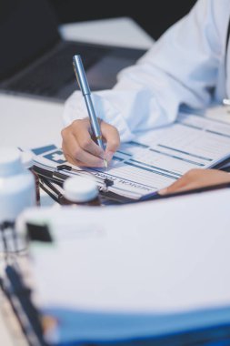 Doktor masasında oturuyor ve hastası için reçete yazıyor.