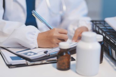 Doktor masasında oturuyor ve hastası için reçete yazıyor.