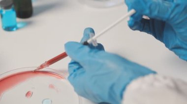 Bilim adamının elinde pipetle kırmızı bir tüp tuttuğu yakın plan.