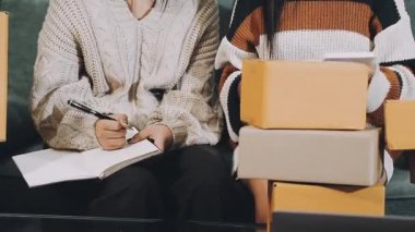 İki Asyalı genç kadın bir kanepede oturuyor ve ellerinde bir defter tutuyorlar.